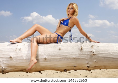 beautiful young adult attractive and sensuality blonde woman in blue bikini posing on a log in the beach