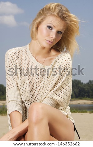 beautiful young adult attractive blonde woman in brown sweater posing on a log in the beach