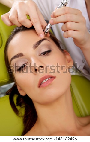 Portrait of attractive beautiful young adult brunette woman having a stimulating facial treatment from a therapist on the table in professional clinic spa