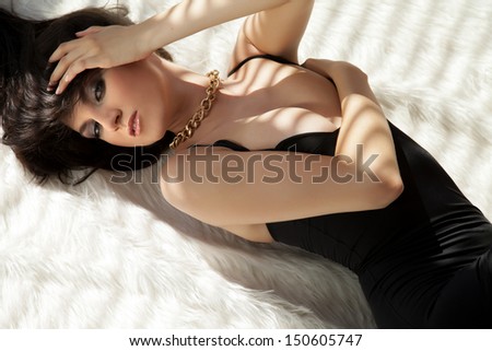 Beautiful and attractive young adult female brunette sensuality woman posing in black dress on white fur