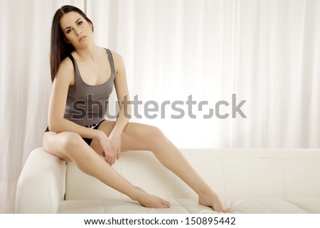 Beautiful and attractive female brunette woman posing in grey shirt on the sofa