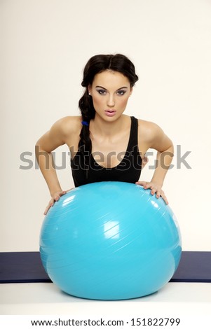 Attractive young brunette sporty woman in black dress with blue fitness ball isolated on white background