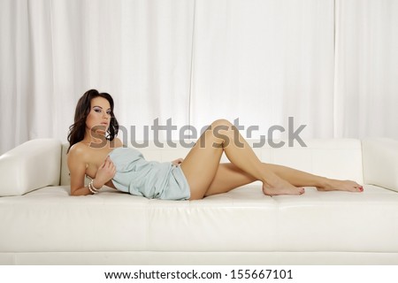 Beautiful and attractive female brunette woman posing in blue blanket on the white sofa