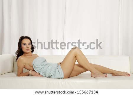 Beautiful and attractive female brunette woman posing in blue blanket on the white sofa