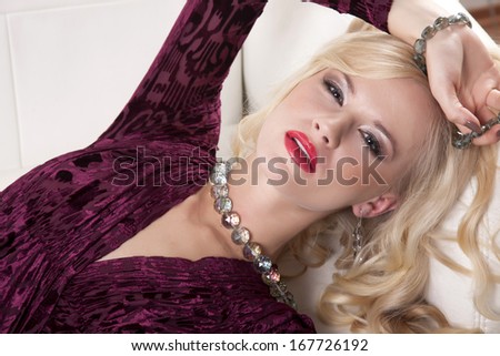 Beautiful and sexy young adult blonde woman wearing elegance fashionable dress in white sofa