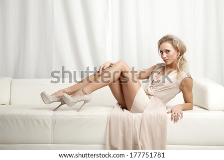 Beautiful and sexy young adult blonde woman wearing elegance fashionable dress in white sofa