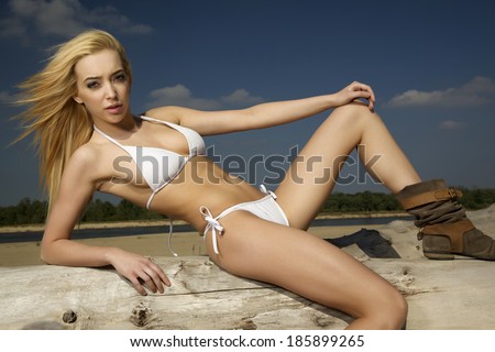 beautiful blonde woman in white bikini posing on a log