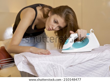 young brunette woman ironing shirt on ironing board