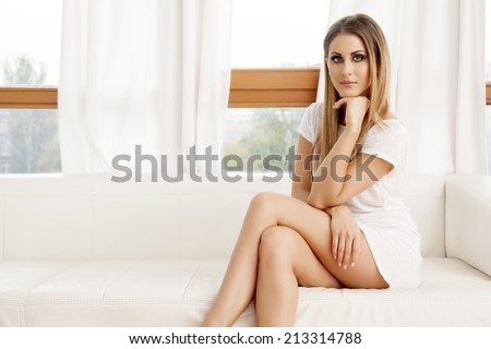 Beautiful and sexy young adult brunette woman wearing elegance fashionable dress in white sofa