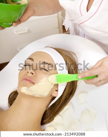 young woman getting beauty skin mask treatment on her face with brush
