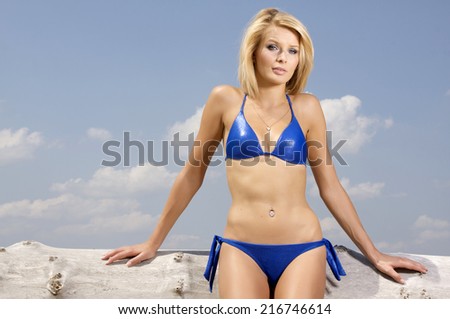 beautiful and attractive sensuality young adult blonde woman in blue bikini posing on a log on a sunny beach