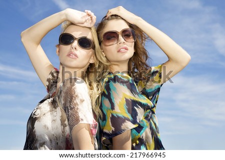 two sensuality beautiful young adult pretty brunette and blonde girl friends in sunglasses and summer dress on background blue sky