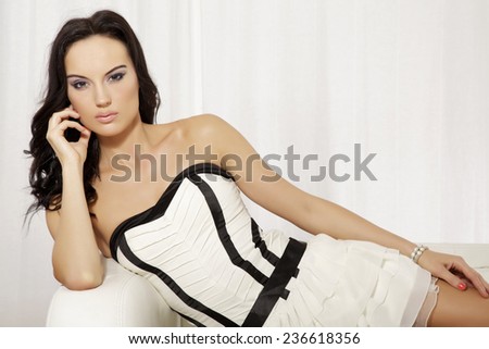 Portrait of beautiful and attractive young adult sensuality and sexy female brunette woman posing in white and black dress on the sofa
