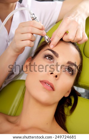 Young adult brunette pretty woman getting laser face treatment in medical spa center, skin rejuvenation concept