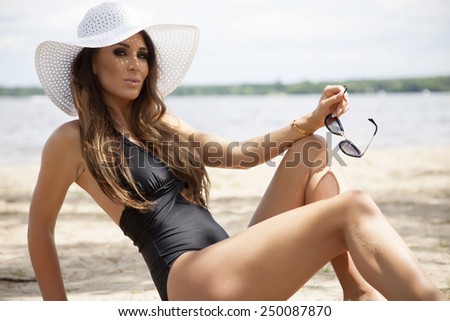 Young adult beautiful sensuality sexy and attractive brunette pretty woman in black swimwear dress and white hat and sunglasses on the sunny beach in summertime