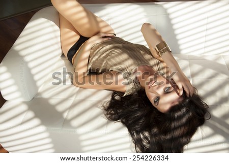 Beautiful sensuality and attractive sexy pretty young adult brunette woman posing in  brown sweater on the white couch in luxury style apartment