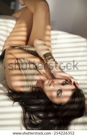 Beautiful sensuality and attractive sexy pretty young adult brunette woman posing in  brown sweater on the white couch in luxury style apartment