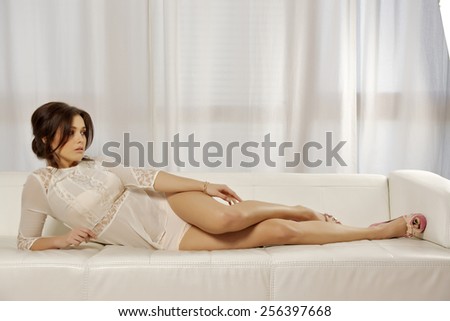Portrait of beautiful and sexy attractive sensuality young adult pretty brunette woman wearing white lingerie dress on the couch in luxury style hotel apartment