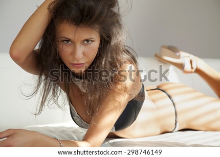 Portrait of a beautiful and sexy attractive young adult pretty brunette woman wearing black lingerie on white couch in window sunlight morning shadow