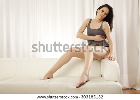 Portrait of a beautiful sensuality and attractive young adult pretty brunette woman posing in grey shirt on the white couch