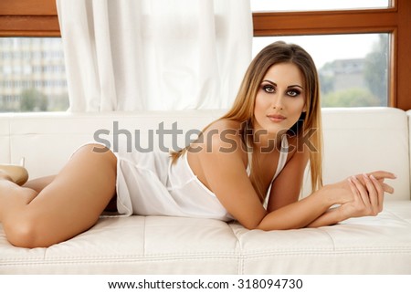 Portrait of a beautiful attractive sensuality and sexy young adult pretty brunette woman wearing white erotic lingerie on the couch in luxury style elegance apartment
