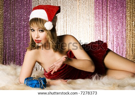 beautiful blonde girl wearing Santa costume holding Christmas present lying on colorful background