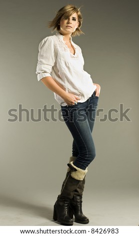 beautiful blonde model wearing white shirt, jeans and boots on grey background