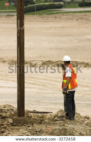 Construction worker overseeing an auger digging a hole at a construction project.