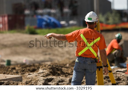 Construction surveyor in orange T-shirt and hardhat giving directions.