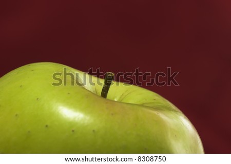 Stem of a green apple against a red background. Focus is on stem with narrow depth of field.
