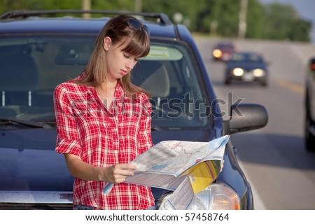 Young woman in front of a car on roadside reading a map