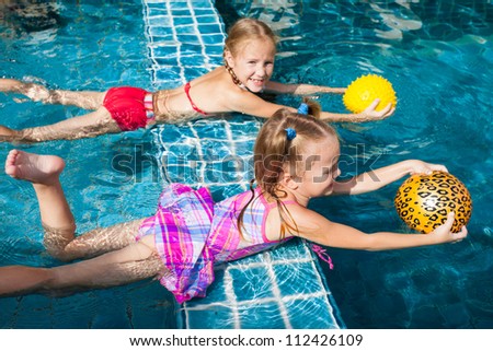 two little girls holding balls in their hands and playing in the pool