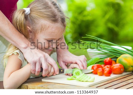 sliced cucumber. Mother teaches daughter  knife cut cucumber