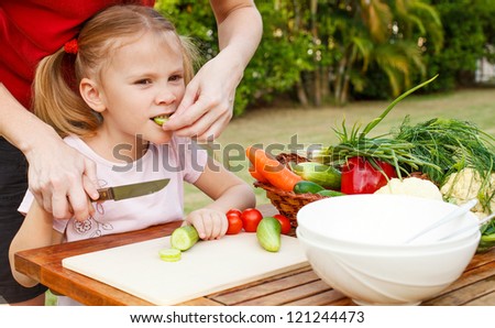 mother teaches daughter  knife cut cucumber