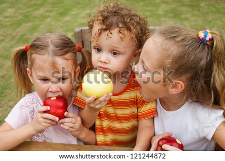 three happy children sitting at the table and eat apples