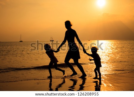 Mother and two kids silhouettes running on beach at sunset
