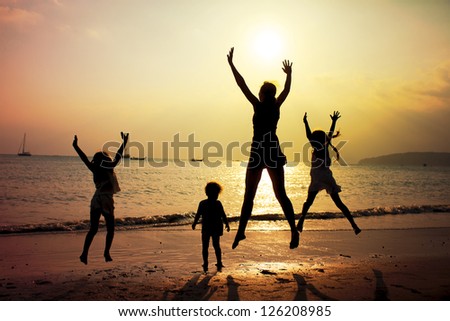 Mother and three kids silhouettes jumping on beach at sunset