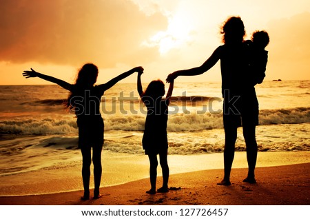 Mother and three kids silhouettes standing on beach at sunset