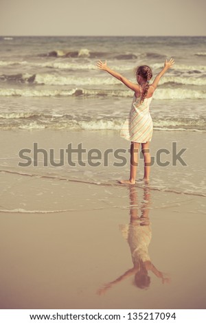 little girl stands on the beach and pulls hands to the sky