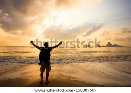 Man with his hands up on the dawn on the beach