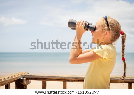 little girl on the beach looking at the sky through binoculars
