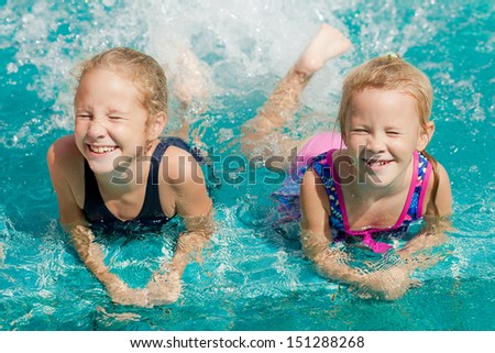 two happy little girls playing around in the pool in the day time