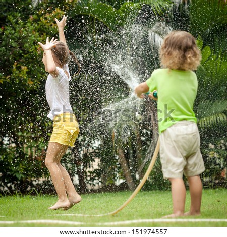 Little Boy Is Pouring A Water From A Hose At His Sister