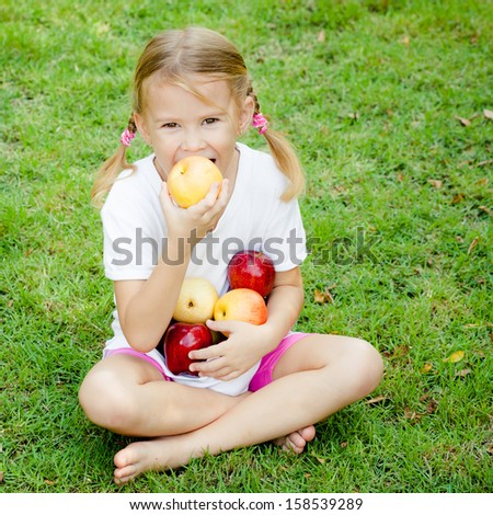 little girl sitting on the grass and holding apples