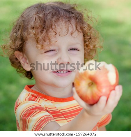 little boy standing on the grass and holding apple