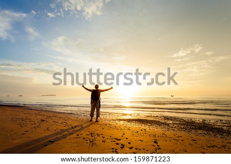 Man with his hands up on the dawn on the beach