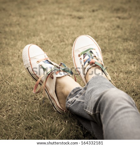 white sneakers on girl legs on grass during sunny serene summer day.