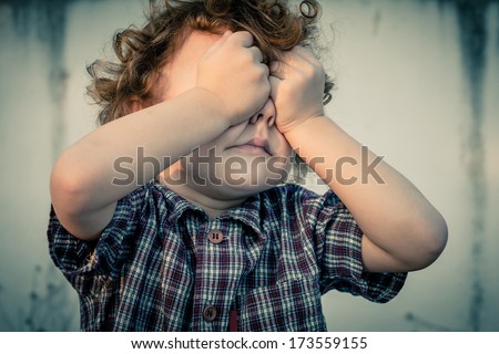 crying little boy covers his face