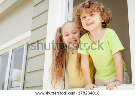 Joyful kids looking out the window at home. Brother And Sister Together Forever