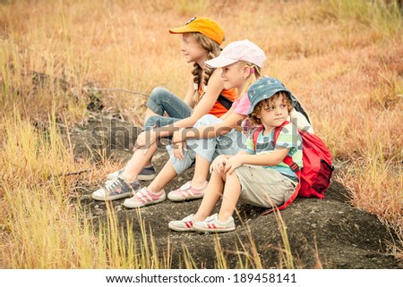 three little kids with backpack sitting on the footpath in the mountains